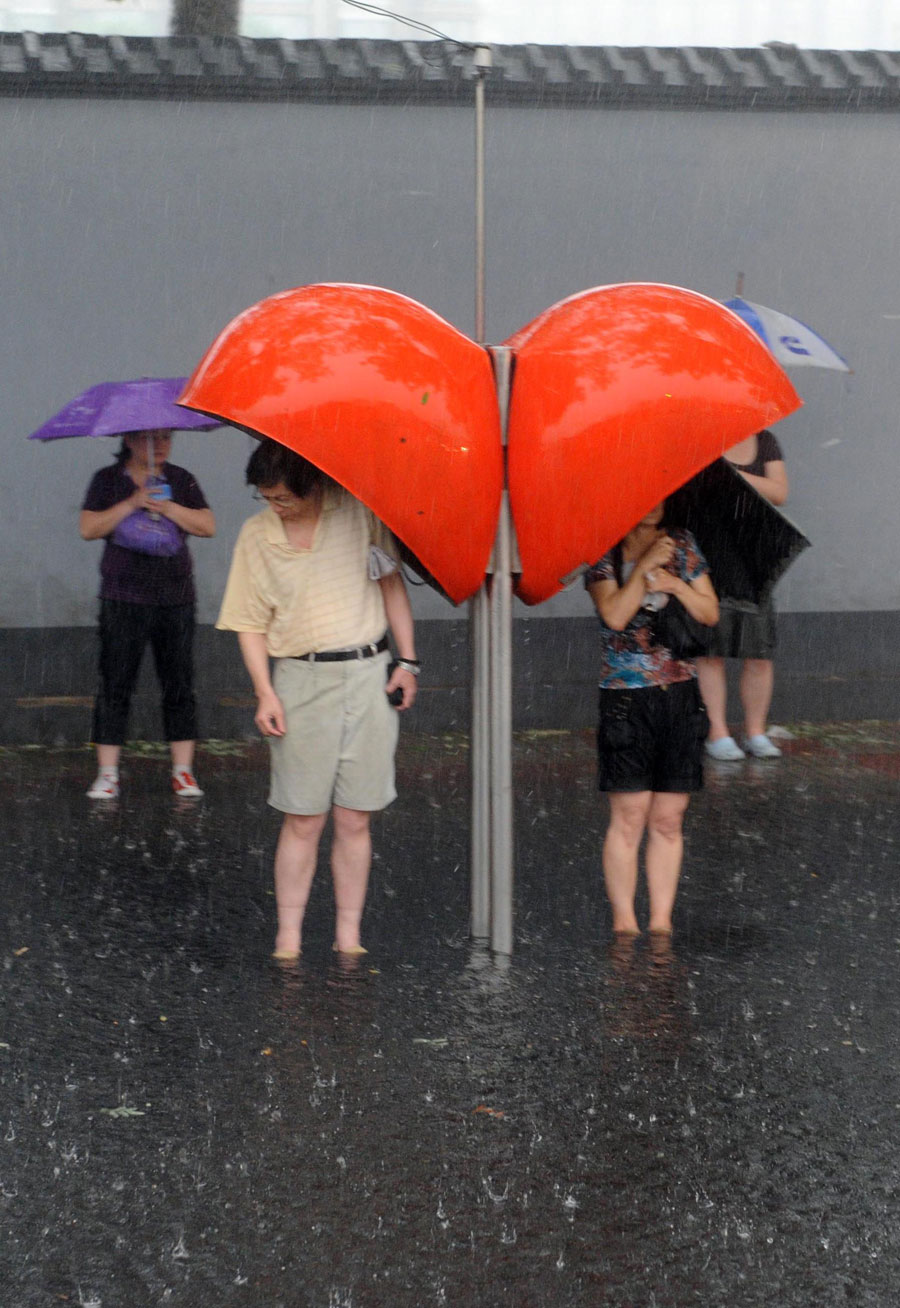 People hide from the rain under telephone booths on a street in Beijing, capital of China, June 23, 2011. Rainstorms pounded the Chinese capital Thursday afternoon. The storms delayed flights, slowed road traffic and disrupted the operation of two subway lines in the afternoon rush hours. [Xinhua]