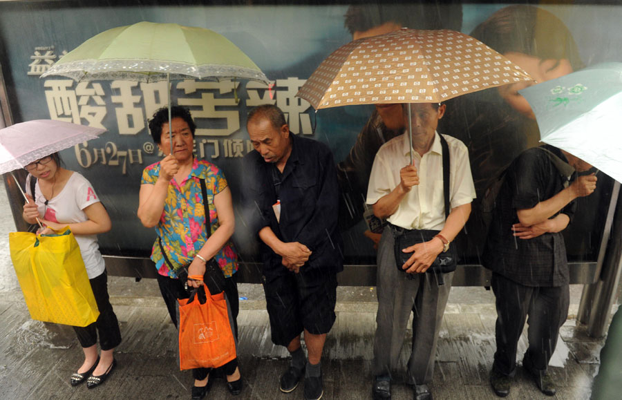 People hide from the rain beside an advertisement box on a street in Beijing, capital of China, June 23, 2011. Rainstorms pounded the Chinese capital Thursday afternoon. The storms delayed over 140 flights, slowed road traffic and disrupted the operation of two subway lines in the afternoon rush hours. [Xinhua]