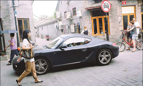 A Porsche car weaves its way through pedestrian traffic in a hutong neighborhood in Beijing. The number of millionaires in China grew by 12 percent to 534,500 last year. [China Daily via agencies]