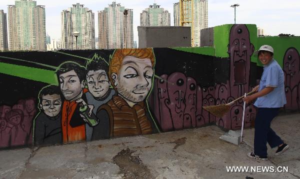 A cleaner walks past a wall with graffiti in Shanghai, east China, June 23, 2011. A 300-meter-long graffiti was unveiled near the Bund in central Shanghai on Thursday. 