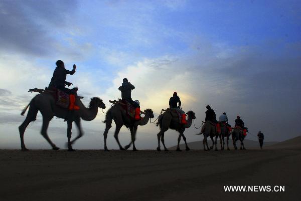 Tourists riding on camels enjoy the sunrise in Mingsha Mountain scenery zone in Dunhuang, northwest China's Gansu Province, June 24, 2011. Tourist volume and tourism industry income of the city reached 482,000 and 410 million RMB yuan (about 63.34 million U.S. dollars) respectively in the first five months of this year, 41 percent and 102.5 percent higher than the same period of the previous year respectively. [Xinhua/Zhang Weixian]