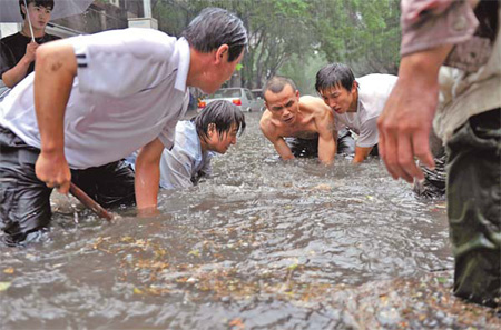 Several men try to move a manhole cover to ease the flood in downtown Beijing on Thursday. [Jin Shuo / China News Service]