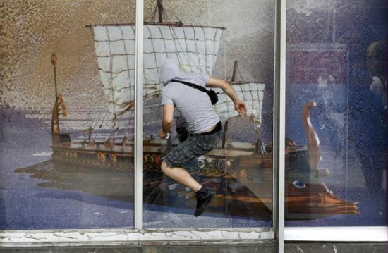 A demonstrator jumps to attempt to break a window displaying an image of an ancient greek galley during protests against austerity measures in Athens, June 28, 2011.