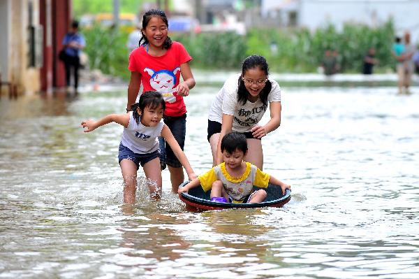 Children frolic in a street of Beigeng Township of Xingcheng County, south China's Guangxi Zhuang Autonomous Region, July 2, 2011. The traffic here has been almost resumed thanks to water recession after being submerged by flood for two days. A flash flood triggered by days of heavy rain submerged here, trapping more than 2,600 residents in their homes for two days, local officials said Friday. [Huang Xiaobang/Xinhua]