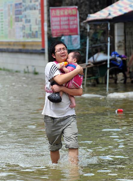 A citizen with a baby in his arms walks in a street of Beigeng Township of Xingcheng County, south China's Guangxi Zhuang Autonomous Region, July 2, 2011. The traffic here has been almost resumed thanks to water recession after being submerged by flood for two days. A flash flood triggered by days of heavy rain submerged here, trapping more than 2,600 residents in their homes for two days, local officials said Friday. [Huang Xiaobang/Xinhua]