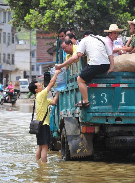 A rescuer passes a bottle of pure water to local citizens in a street of Beigeng Township of Xingcheng County, south China's Guangxi Zhuang Autonomous Region, July 2, 2011. The traffic here has been almost resumed thanks to water recession after being submerged by flood for two days. A flash flood triggered by days of heavy rain submerged here, trapping more than 2,600 residents in their homes for two days, local officials said Friday. [Huang Xiaobang/Xinhua]