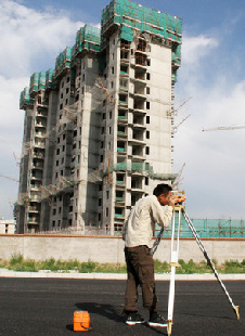 A surveyor at work outside a property in Beijing. Property companies are now under pressure to cut prices of new homes to ride out tightening measures. [China Daily]