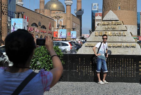 A tourist poses for photos at the International Grand Bazaar in Urumqi, capital of northwest China's Xinjiang Uygur Autonomous Region, July 4, 2011. The International Grand Bazaar in Urumqi, trading a wide range from handicraft items to fruits and fashion clothing, has become the largest collecting and distributing center for goods in Central Asia. [Xinhua/Wang Fei] 