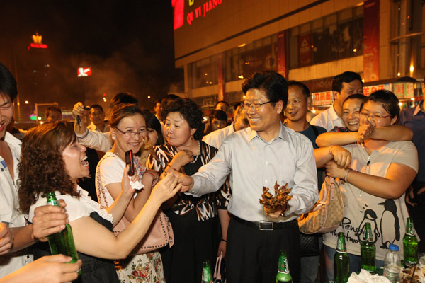 Zhang Chunxian (center), Party chief of the Xinjiang Uygur autonomous region, on Monday offers lamb kebabs to local residents who were having dinner at a food court in Urumqi.