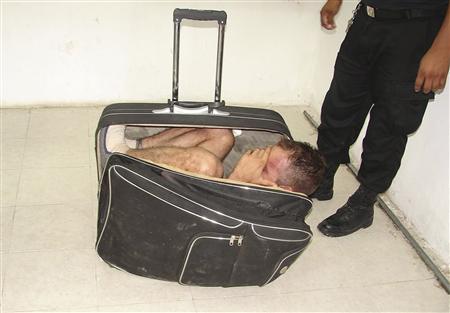 Prison guards stand around inmate Juan Ramirez as he hides in a suitcase during an escape attempt from a prison in Chetumal, July 2, 2011. [Reuters]