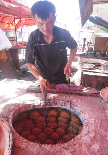 A baker pulls sesame bagels out of a tandoori oven in Kashgar, Xinjiang Uyghur Autonomous Region. [Photo:CRIENGLISH.com]