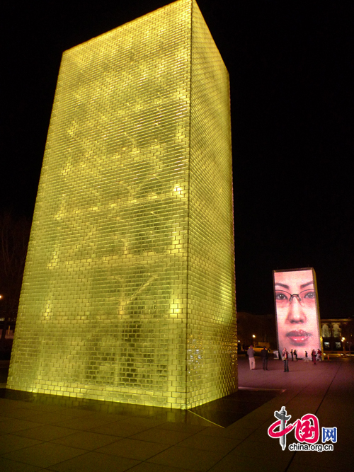 The Crown Fountain is an interactive work of public art and video sculpture in Millennium Park in Chicago, US. It is composed of a black granite reflecting pool placed between a pair of transparent glass brick towers. The towers are 50 feet (15 m) tall, and use light-emitting diodes behind the bricks to display digital videos on their inward faces. [Photo by Xu Lin/China.org.cn]