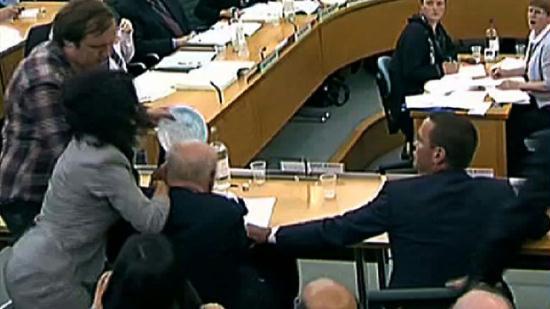 Shows a man (Top L) hitting News Corporation Chief Rupert Murdoch (2nd Row Seated L) in the face with a plate of foam as he and son James (2nd Row Seated R) give evidence to a Parliamentary Select Committee on the phone hacking scandal.