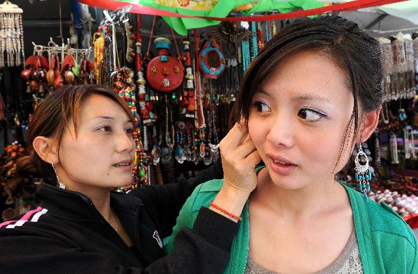 A girl (R) tries a pair of earrings in a shop on Barkhor Street in Lhasa, capital of southwest China's Tibet Autonomous Region, July 24, 2011. A large number of tourists poured into Tibet during the summer season, as the region is celebrating the 60th anniversary of its peaceful liberation. The region received 2.25 million tourists in the first half of this year, 24.8 percent more than the same period of last year. [Xinhua/Chogo] 