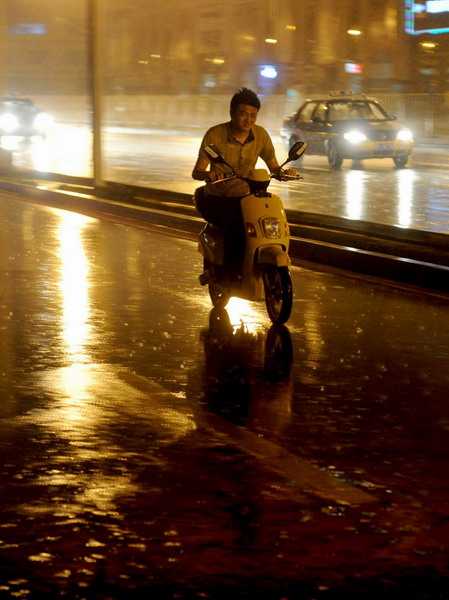 A motorcyclist rides in heavy rain Tuesday night in downtown Beijing. [Photo/Xinhua] 