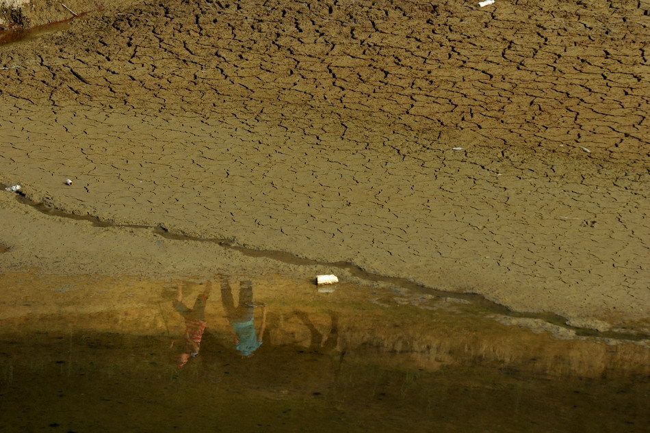 People are reflected upon the leftover water in a reservoir in Qianxi County, southwest China&apos;s Guizhou Province, July 28, 2011. Serious drought hit Guizhou in July. [Xinhua] 