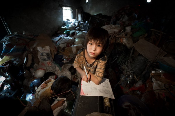 Sun Wanli does homework among rubbish in the family's house in Woyang county, East China's Anhui province, July 27, 2011. [Photo/Xinhua]