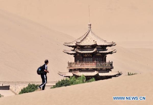 A tourist visits the scenic spot of Mingsha Mountain and Crescent Moon Lake in Dunhuang City, northwest China's Gansu Province, July 29, 2011. This scenic spot received near 300,000 tourists in the past seven months, reaching a new high in recent years. [Xinhua/Gao Jianjun]