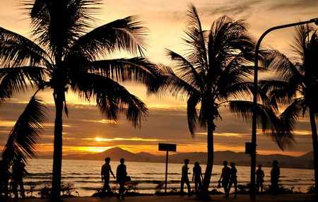 Tourists walk under sunset in Sanya city, south China's Hainan province, July 20, 2011.[