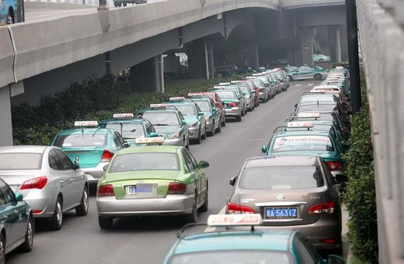Local residents pass by taxis parked along a street on Monday. The drivers of the cabs have gone on strike over rising gasoline prices and road congestion in Hangzhou, capital of East China's Zhejiang province. 