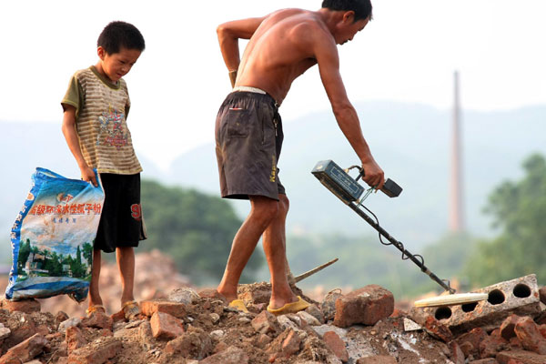 Xiong Sansan follows his father with a bag to collect scrap irons at a building site in Liuzhou city, South China's Guangxi Zhuang autonomous region, July 29, 2011.