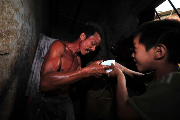Xiong Sansan gives a bowl of water to his father who just came back from working in Baisha, an urban village in Liuzhou city, South China's Guangxi Zhuang autonomous region, July 29, 2011. 