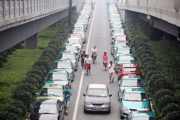 Local residents pass by taxis parked along a street on Monday. The drivers of the cabs have gone on strike over rising gasoline prices and road congestion in Hangzhou, capital of East China's Zhejiang province. [Photo/China Daily] 