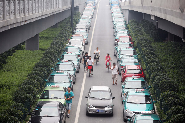 Local residents pass by taxis parked along a street on Monday. The drivers of the cabs have gone on strike over rising gasoline prices and road congestion in Hangzhou, capital of East China's Zhejiang province. [Photo/China Daily]