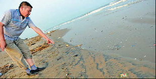 A man points to oil on the beach in Laoting county, Hebei province, on July 26. The oil is suspected to have come from the oilfield spill in Bohai Bay. [China Daily] 