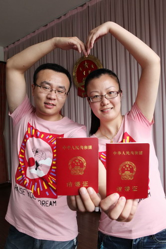 A newly-wed couple poses with their marriage certificates at a marriage registry office in Ganyu county, Jiangsu province, Aug 6, 2011.
