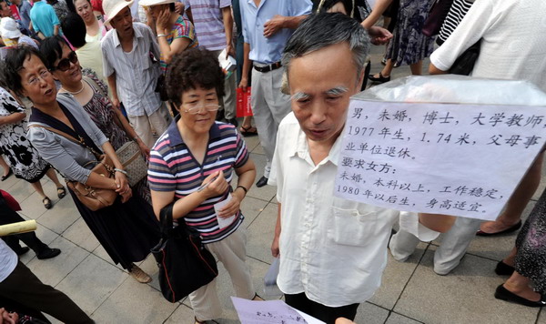 A man holds up a sign displaying his unmarried son's information at a matchmaking fair held by the local Women's Federation in Harbin, capital of Northeast China's Heilongjiang province, Aug 6, 2011. 