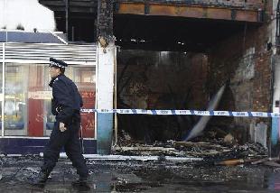 A police officer cordons off shops set alight and burned during riots in Tottenham, north London, August 7, 2011. Rioters throwing petrol bombs battled police in a economically deprived district of London overnight, setting patrol cars, buildings and a double-decker bus on fire in some of the worst disorder seen in the capital for recent years. [Xinhua]