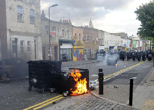 Policemen press forward on a street in Hackney, east London, Britain, Aug. 8, 2011. Rioting starting late Saturday appears spreading across London on Monday, with vandalising, arson and looting taking place in various London communities. [Xinhua]