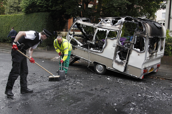 A police officer and council worker clean the pavement from where they had moved the burned out shell of a camper, which was torched during overnight rioting and looting in the neighbourhood of Toxteth in Liverpool, northern England August 10, 2011 [Xinhua]