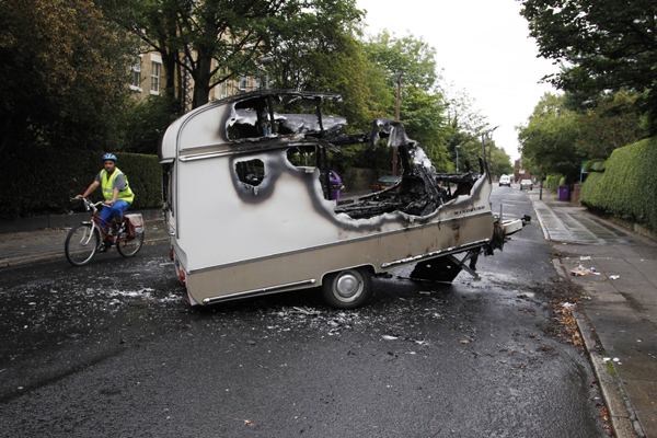 A cyclist passes the burned out shell of a camper after overnight rioting and looting in the neighbourhood of Toxteth in Liverpool, northern England August 10, 2011. [Xinhua]