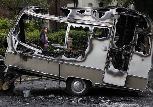 A woman passes the burned out shell of a camper after overnight rioting and looting in the neighbourhood of Toxteth in Liverpool, northern England August 10, 2011. [Xinhua]