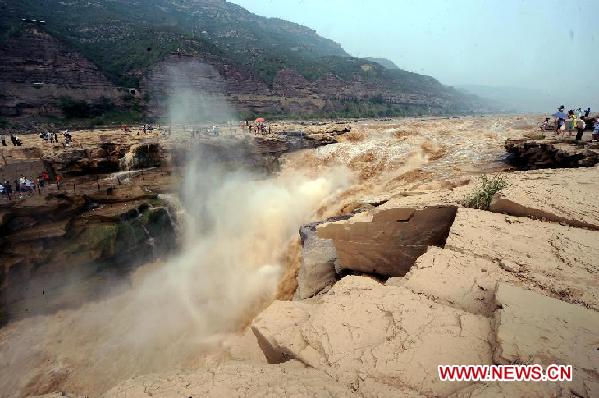 Tourists standing on rocks view the Hukou Cataract on the Yellow River in Jixian County, north China's Shanxi Province, on Aug. 15, 2011. Tourist arrivals at the scenic spot pick up steadily as the water volume of the waterfall increases during the annual flood season. [Xinhua/Fan Minda]