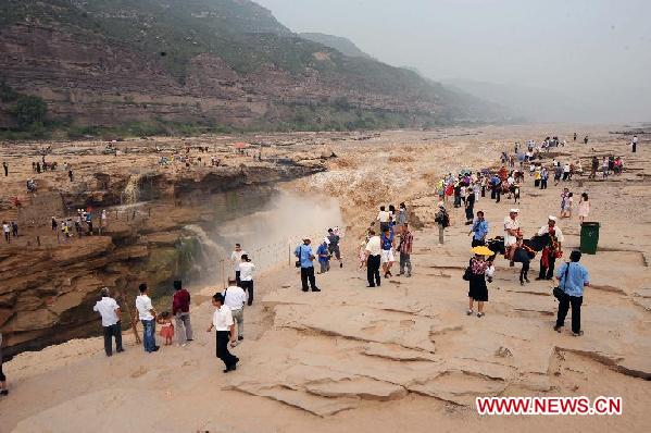 Tourists standing on rocks view the Hukou Cataract on the Yellow River in Jixian County, north China's Shanxi Province, on Aug. 15, 2011. Tourist arrivals at the scenic spot pick up steadily as the water volume of the waterfall increases during the annual flood season. [Xinhua/Fan Minda]