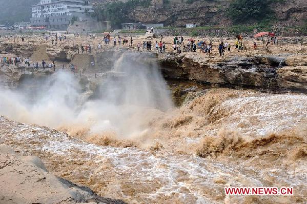 Tourists standing on rocks view the Hukou Cataract on the Yellow River in Jixian County, north China's Shanxi Province, on Aug. 15, 2011. Tourist arrivals at the scenic spot pick up steadily as the water volume of the waterfall increases during the annual flood season. [Xinhua/Li Xiaoguo] 