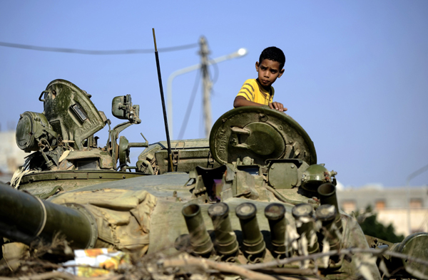 A boy sits on a destroyed tank in a place 40 kilometers west away from Libyan capital Tripoli on August 20, 2011. 