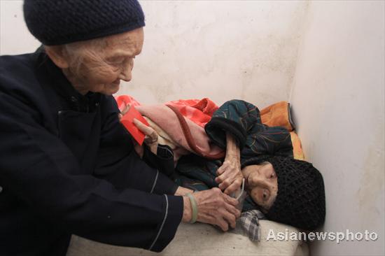 Huang Magan (left), 106, hands water to her long-term companion and her husband's second wife, 103-year-old Huang Maxue, who is sick, at their home in Ping'an village, Bama Yao autonomous county, South China's Guangxi Zhuang autonomous region, August 21, 2011. 