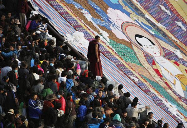 A Tibetan monk stands between tourists and a giant thangka, a religious silk embroidery or painting unique to Tibet, during the Shoton Festival at Drepung Monastery on the outskirts of Lhasa, August 29, 2011.