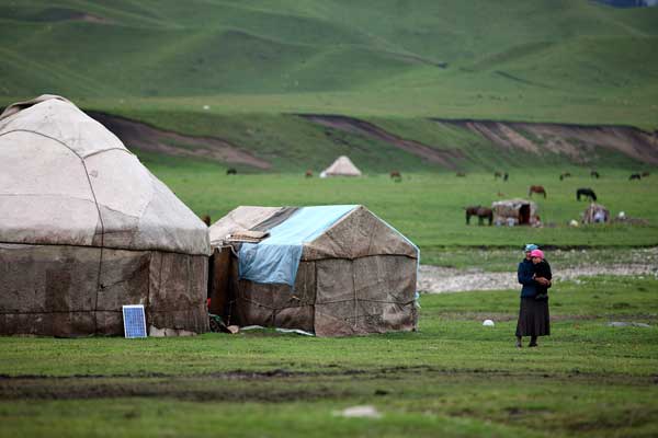 A Kazak mother holding her child stands beside her yurt home. [Photo:CRIENGLISH.com/Huang Wenhua]