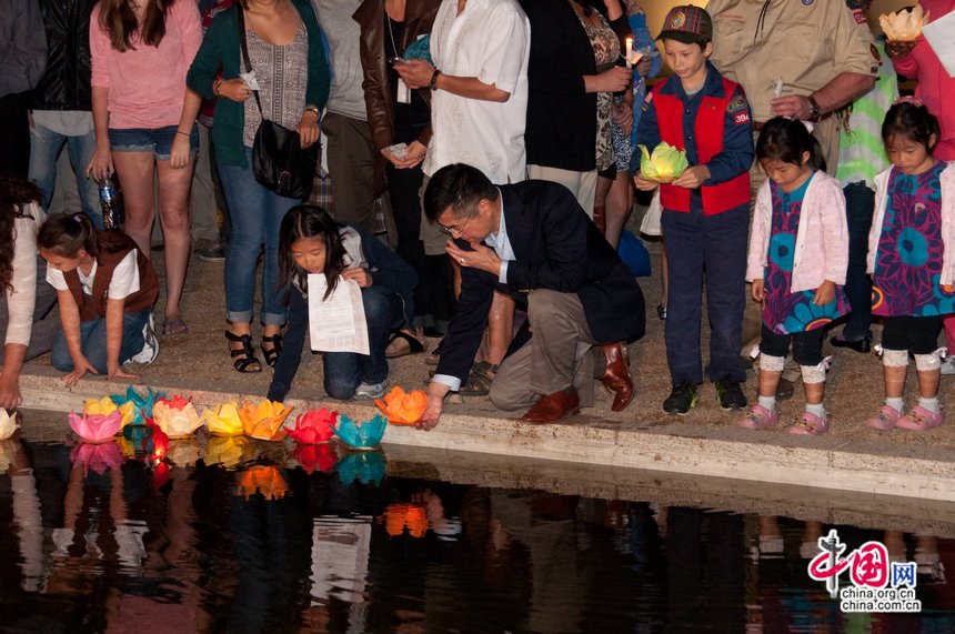 Gary Locke, US ambassador to China helps a girl set off a lotus lantern in a pond as a means to show their emotions for the deceased lives in the 911 attacks. [Pierre Chen / China.org.cn]