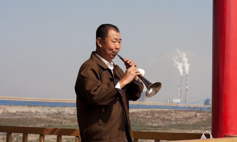 Zhang Jian Hua plays a tune above the mine he used to work in. (Image: Radio86)