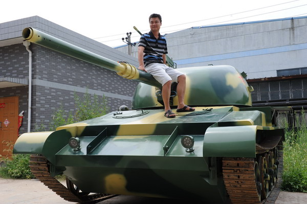 Hao Jinxi, owner of a factory that produces imitation trains, sits on a life-size model of a T-62 tank, his newest product, in Yuhang, Zhejiang province. [Photo/provided to China Daily]