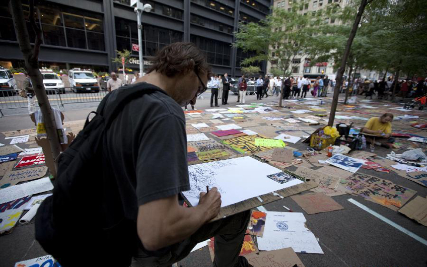 An artist creates in front of placards at a plaza near Wall Street in New York, the United States, on Sept. 27, 2011. After several streets around the Wall Street have been blockaded since Sept. 16, protesters pitched their tents at the Bowling Green and Battery Park to continue their demonstration.