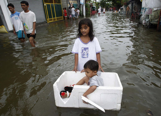 A girl uses a styrofoam box to help her younger brother cross floodwaters brought by Typhoon Nesat, locally known as Typhoon Pedring, in Dampalit town, Malabon city, north of Manila Sept 28, 2011. [China Daily] 