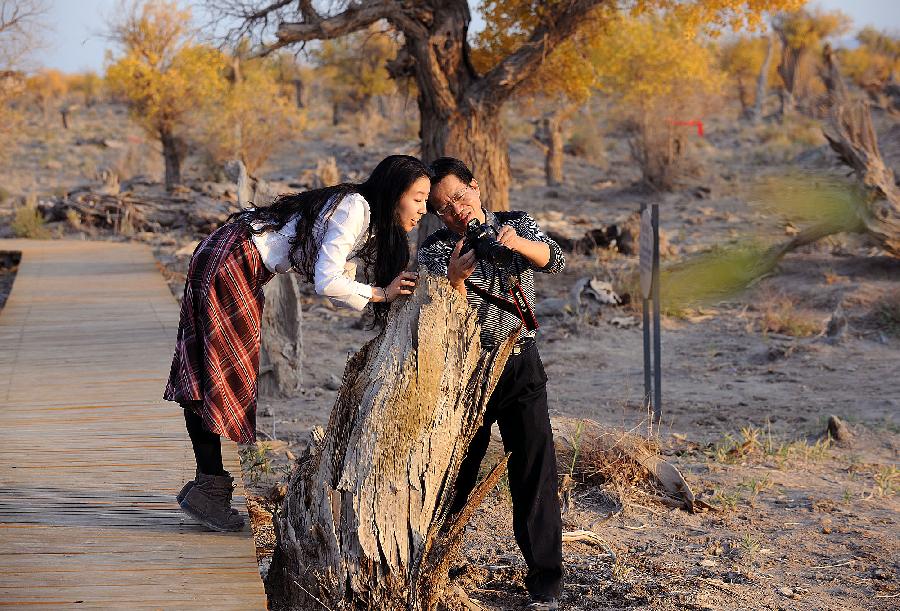 Two visitors look at photos taken in the populus euphratica forest in Hami, northwest China's Xinjiang Uygur Autonomous Region, Oct. 6, 2011. The golden leaves and sunshine here in autumn have attracted lots of tourists. [Xinhua/He Junchang]