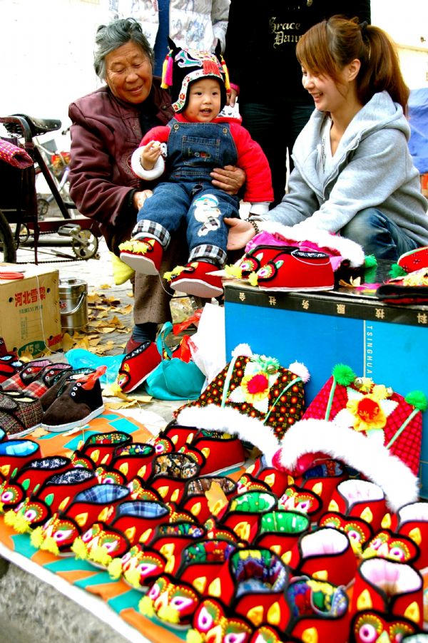 Gao Qinying (1st L) sales tiger boots and hats in Tancheng County of Linyi City in east China's Shandong Province, Oct. 5, 2011. 